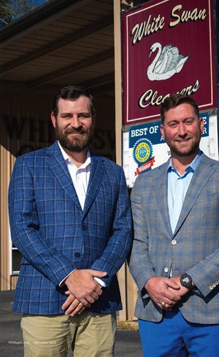 Two men in plaid jackets stand in front of a building with a "White Swan Cleaners" sign and a "Best of" award plaque visible behind them.