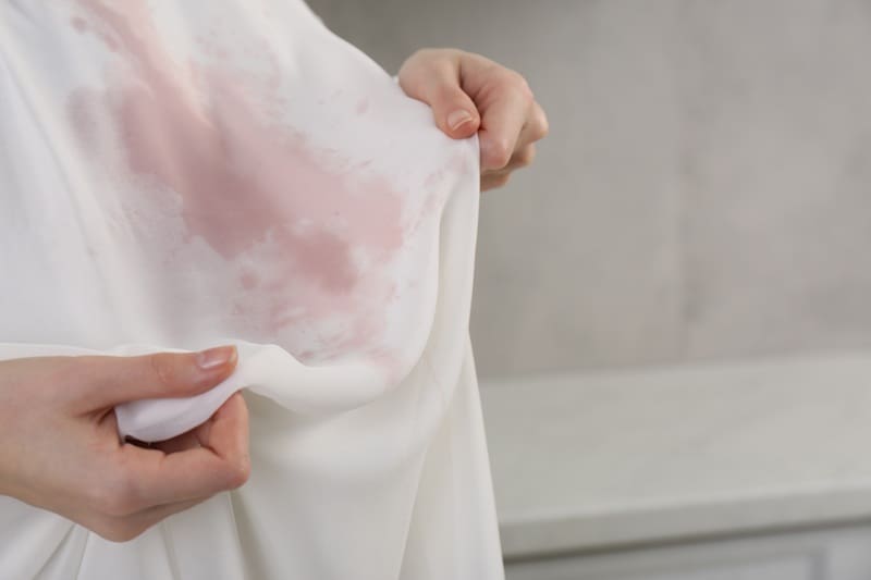 Person holding a white fabric stained with a large pinkish-red mark, inspecting the stain.